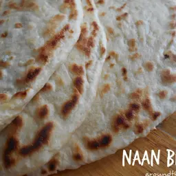 Kilka świeżo upieczonych placków naan, lekko przypieczonych, ułożonych na drewnianym blacie. Idealne do curry lub jako samodzielna przekąska.
