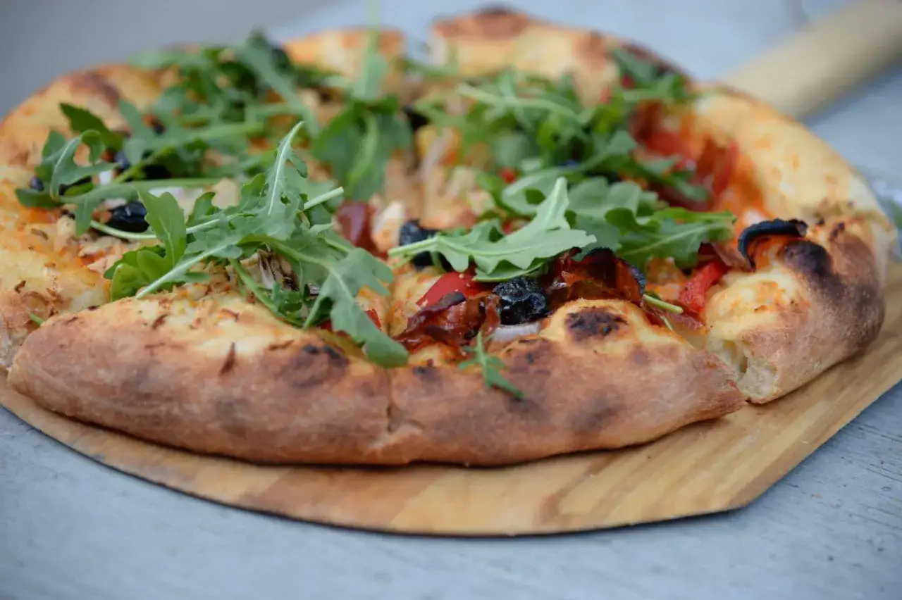 Pyszna pizza na cienkim cieście z rukolą, oliwkami i papryką, podana na drewnianej desce.