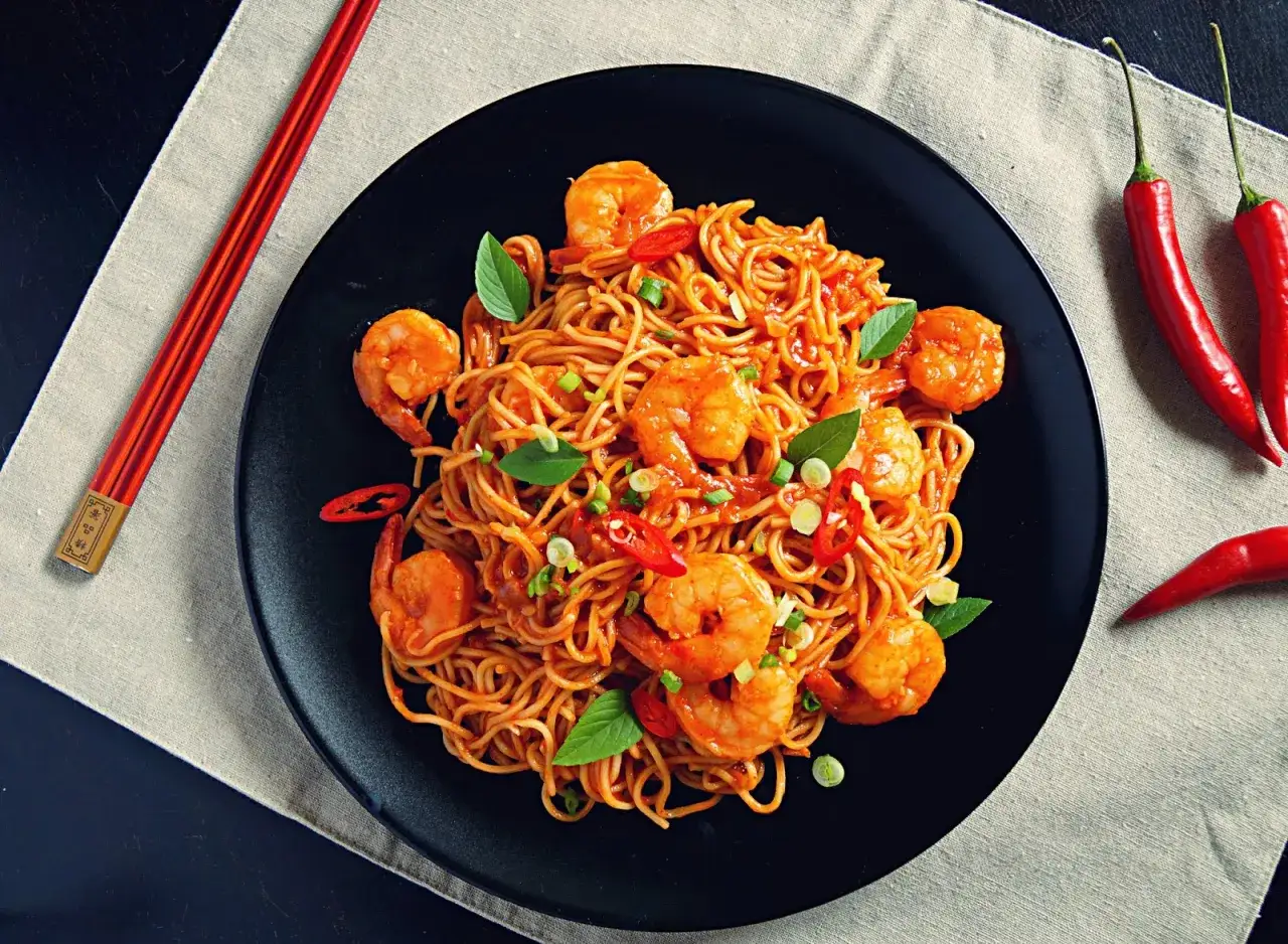 Apetyczny makaron chiński z krewetkami, ozdobiony bazylią i papryczkami chili. Gotowy do jedzenia pałeczkami.