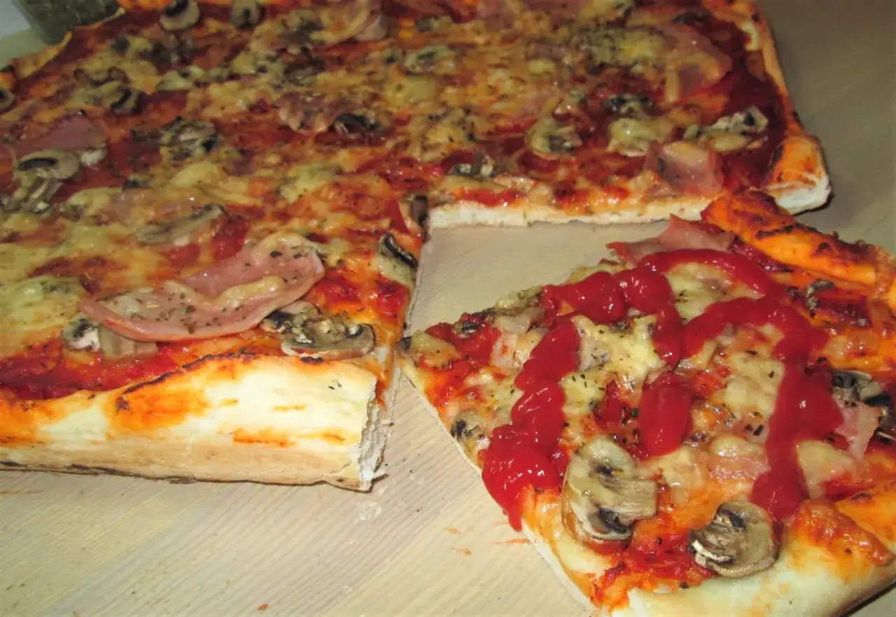 Pyszna pizza na cienkim cieście z szynką i pieczarkami, polana ketchupem. Idealna na szybki obiad.